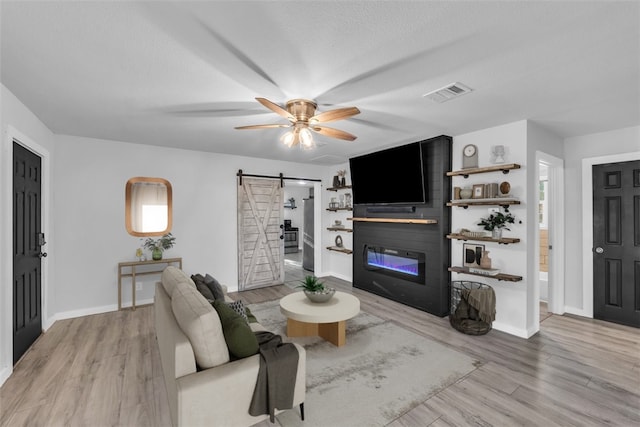 living room with ceiling fan, a barn door, and light hardwood / wood-style floors