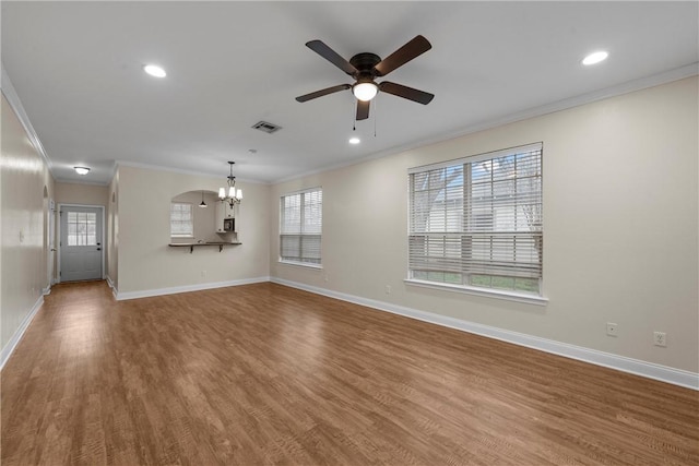 unfurnished living room with hardwood / wood-style flooring, ornamental molding, ceiling fan with notable chandelier, and plenty of natural light