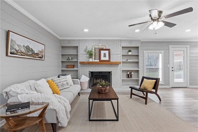 living room with a brick fireplace, light hardwood / wood-style flooring, ornamental molding, built in features, and ceiling fan