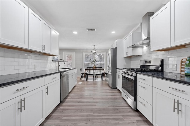 kitchen with wall chimney range hood, sink, appliances with stainless steel finishes, dark stone countertops, and white cabinets