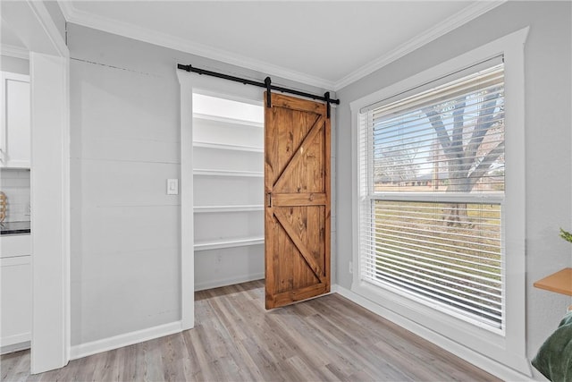 interior space with ornamental molding, a barn door, light hardwood / wood-style floors, and a wealth of natural light