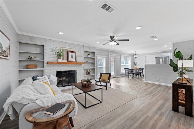 living room with light wood-type flooring, ornamental molding, built in features, ceiling fan, and a fireplace