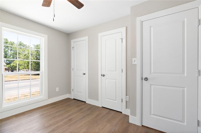 unfurnished bedroom featuring ceiling fan, wood-type flooring, and multiple windows