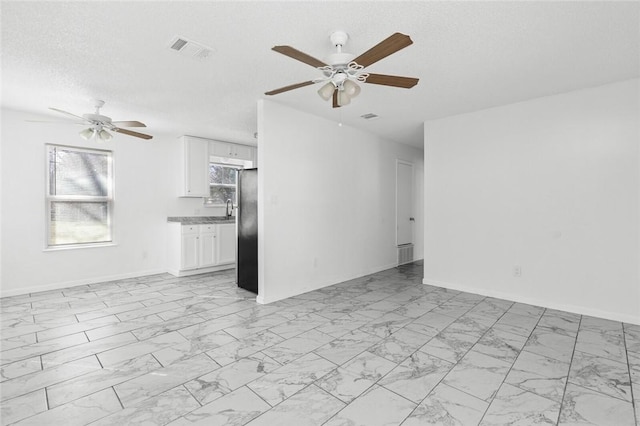 unfurnished living room with ceiling fan and a textured ceiling