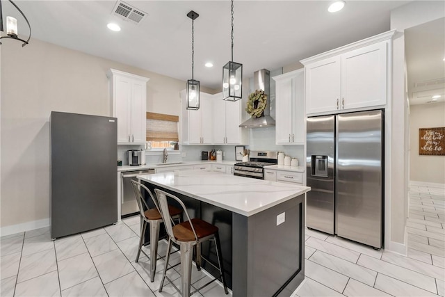 kitchen featuring wall chimney range hood, hanging light fixtures, stainless steel appliances, white cabinets, and a kitchen island