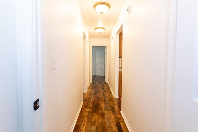 corridor featuring dark wood-type flooring and baseboards