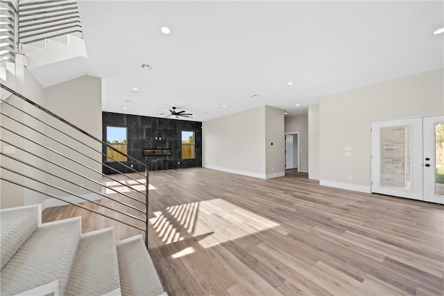 unfurnished living room featuring a tiled fireplace, ceiling fan, french doors, and light wood-type flooring