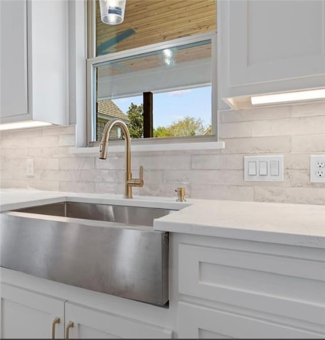 room details featuring sink, white cabinets, and decorative backsplash