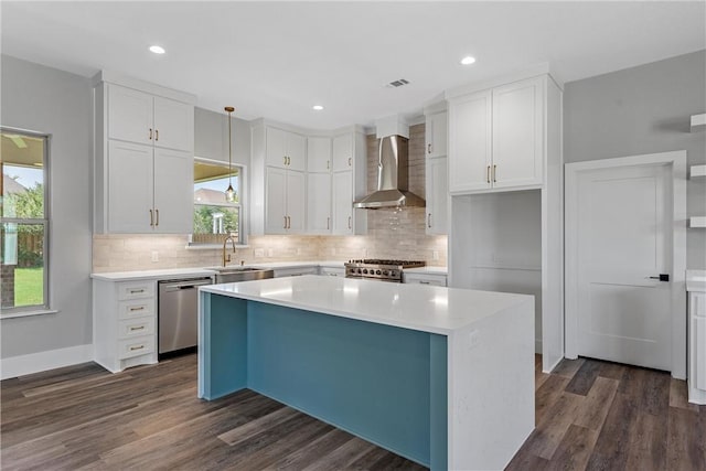 kitchen featuring wall chimney range hood, dishwasher, a kitchen island, and white cabinets