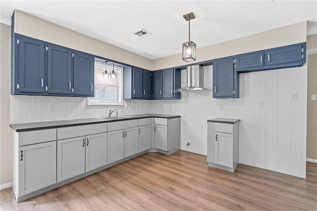 kitchen with blue cabinetry, sink, wall chimney exhaust hood, light hardwood / wood-style flooring, and decorative light fixtures