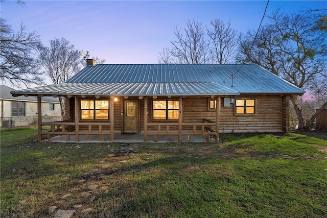 back house at dusk featuring a patio area and a lawn