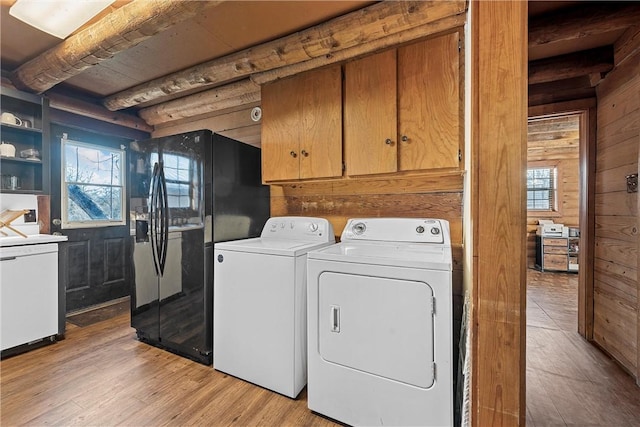 laundry room with light wood-type flooring, washing machine and dryer, cabinets, and wood walls