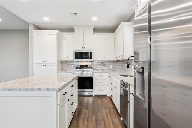 kitchen featuring light stone countertops, appliances with stainless steel finishes, a kitchen island, dark hardwood / wood-style floors, and white cabinetry