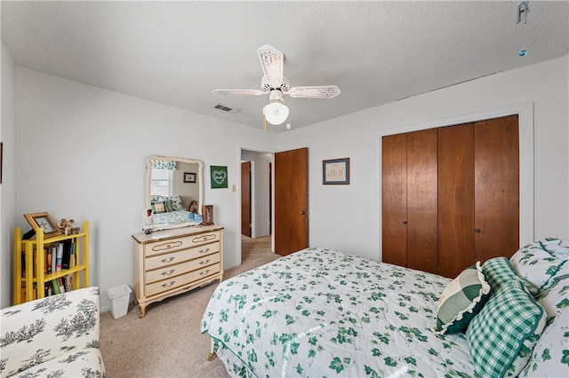 bedroom featuring ceiling fan, light colored carpet, a closet, and a textured ceiling