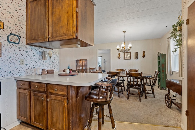 kitchen featuring a breakfast bar area, hanging light fixtures, kitchen peninsula, light carpet, and an inviting chandelier