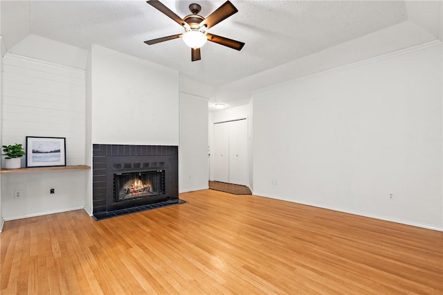 unfurnished living room featuring ceiling fan, a fireplace, a textured ceiling, and light wood-type flooring