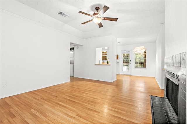 unfurnished living room with a textured ceiling, light wood-type flooring, a brick fireplace, and ceiling fan