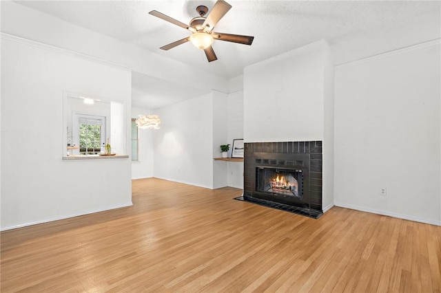 unfurnished living room with a textured ceiling, ceiling fan with notable chandelier, a fireplace, and light hardwood / wood-style flooring