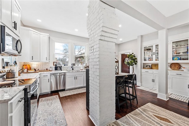 kitchen with ornate columns, white cabinetry, dark hardwood / wood-style floors, stainless steel appliances, and light stone countertops