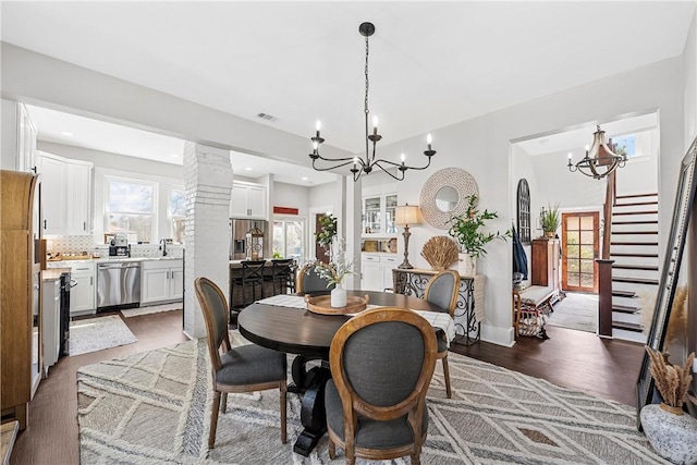 dining space with ornate columns, dark wood-type flooring, sink, and a notable chandelier