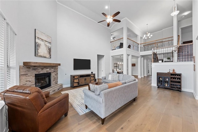 living room with a stone fireplace, a towering ceiling, light hardwood / wood-style floors, ceiling fan with notable chandelier, and ornamental molding