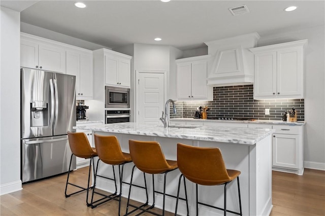 kitchen featuring white cabinets, a center island with sink, appliances with stainless steel finishes, and light hardwood / wood-style flooring