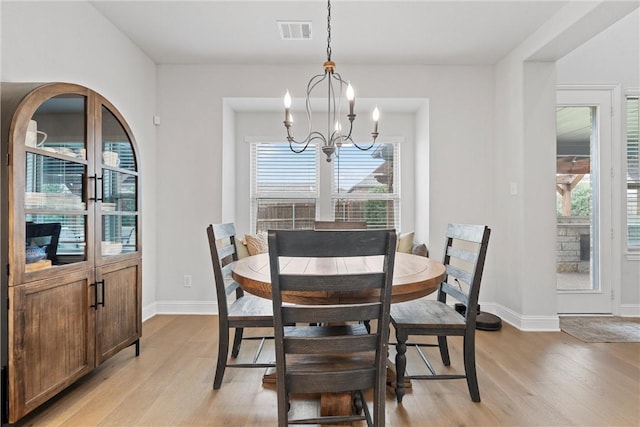 dining room featuring light wood-type flooring, a healthy amount of sunlight, and a notable chandelier