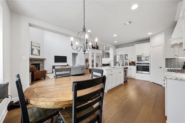 dining room featuring a stone fireplace, sink, a chandelier, and hardwood / wood-style flooring