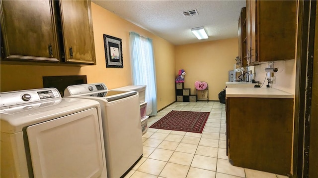 clothes washing area featuring cabinets, light tile patterned floors, a textured ceiling, and washing machine and clothes dryer