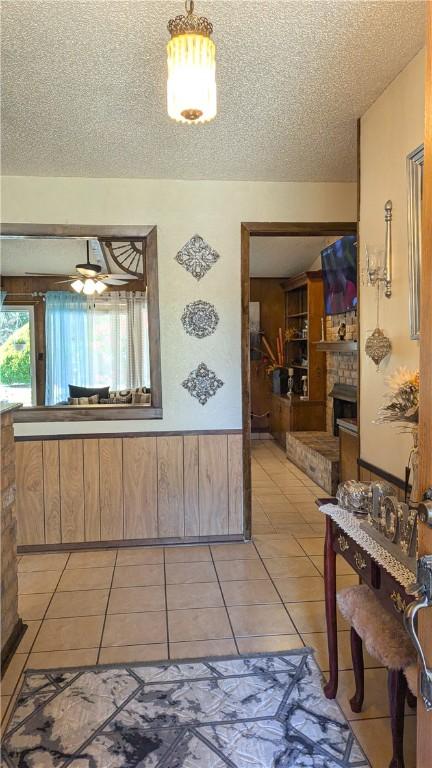 interior space featuring ceiling fan, a textured ceiling, wooden walls, a fireplace, and light tile patterned flooring