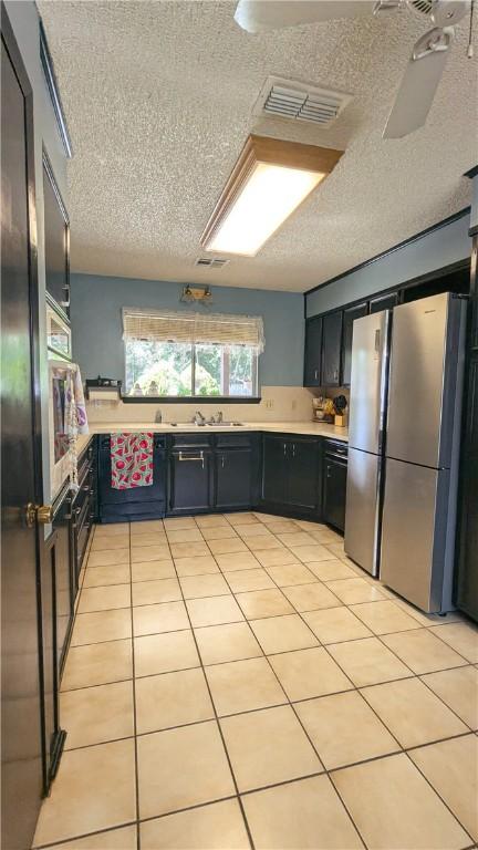 kitchen featuring stainless steel refrigerator, sink, light tile patterned floors, and a textured ceiling