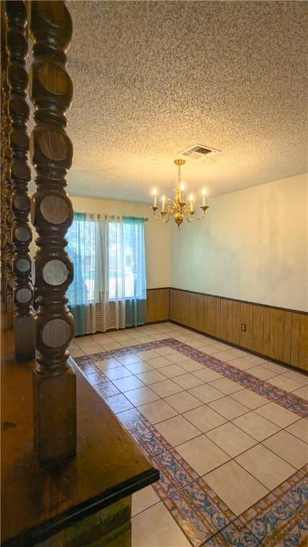 spare room featuring a chandelier, a textured ceiling, wooden walls, and tile patterned flooring