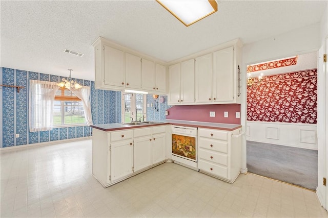 kitchen featuring a textured ceiling, kitchen peninsula, dishwasher, pendant lighting, and white cabinets