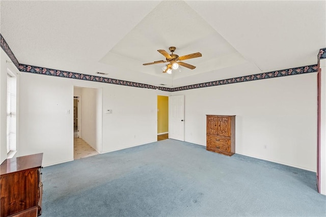 spare room with ceiling fan, a tray ceiling, and carpet