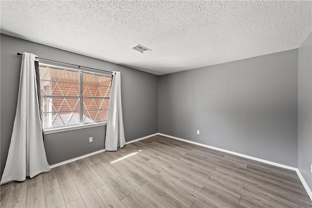 spare room with a textured ceiling and light hardwood / wood-style floors