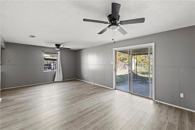 empty room with ceiling fan, a wealth of natural light, and light wood-type flooring