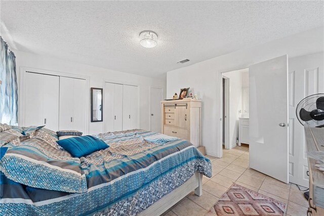 bedroom with multiple closets, light tile patterned floors, and a textured ceiling