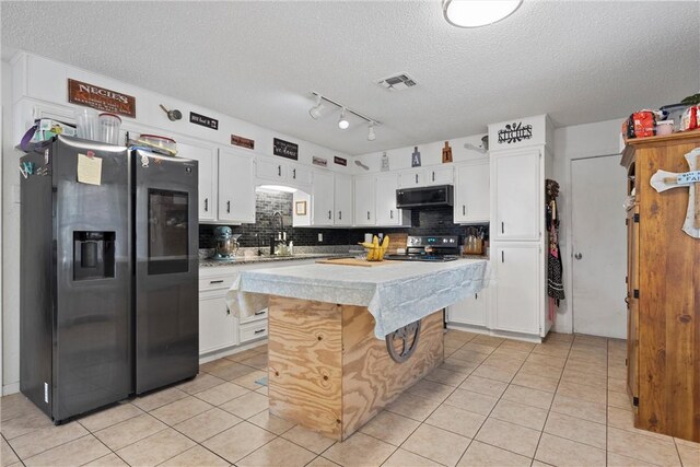 kitchen with a kitchen island, light tile patterned flooring, backsplash, stainless steel fridge, and white cabinets