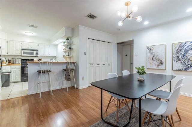 dining area with baseboards, light wood-type flooring, visible vents, and an inviting chandelier