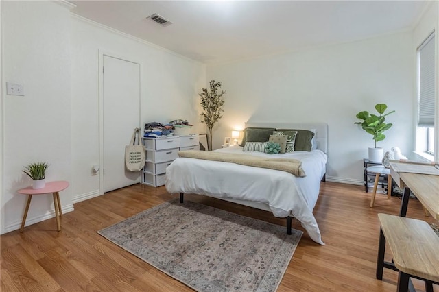 bedroom with baseboards, visible vents, wood finished floors, and ornamental molding