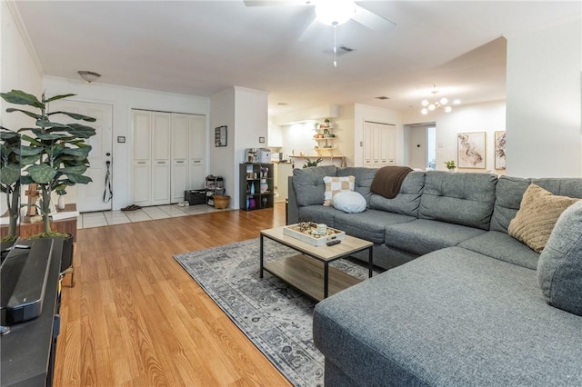 living area featuring light wood finished floors, visible vents, ornamental molding, and ceiling fan with notable chandelier