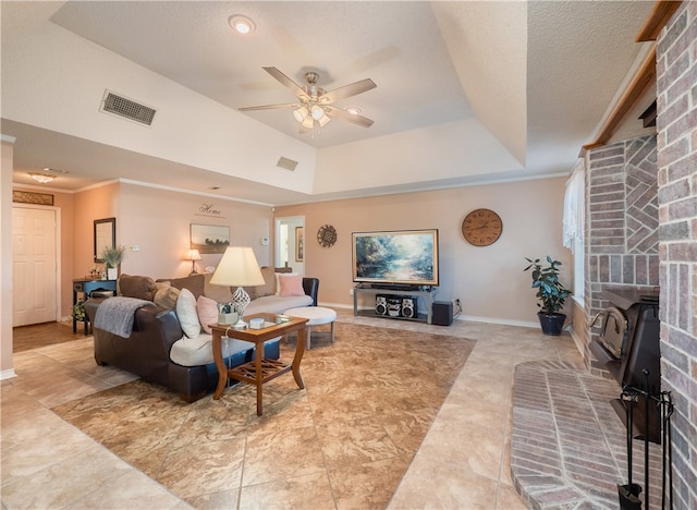 living room with a brick fireplace, a textured ceiling, a raised ceiling, and ceiling fan