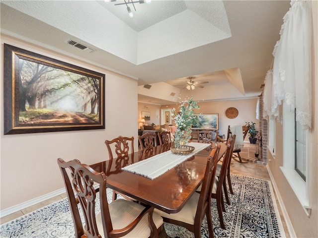 dining room with ceiling fan, tile patterned floors, a raised ceiling, and a textured ceiling