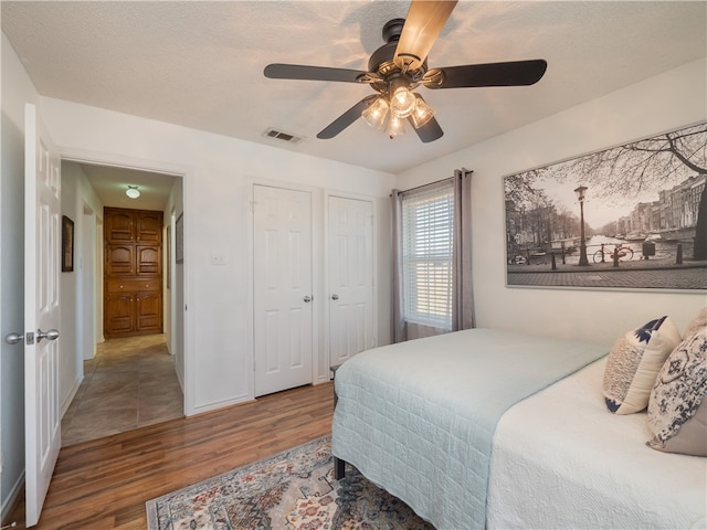 bedroom featuring hardwood / wood-style flooring, multiple closets, a textured ceiling, and ceiling fan