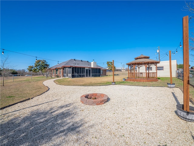 rear view of property featuring a fire pit, a yard, a gazebo, and a sunroom