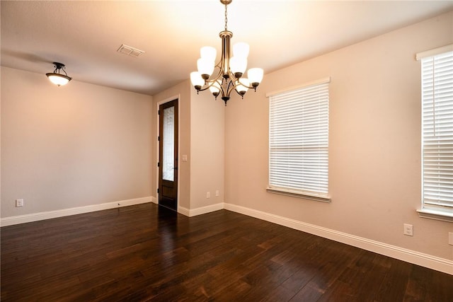 spare room with dark hardwood / wood-style floors and an inviting chandelier