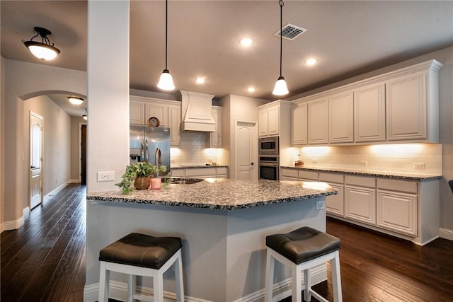 kitchen with tasteful backsplash, premium range hood, stainless steel appliances, white cabinets, and light stone counters