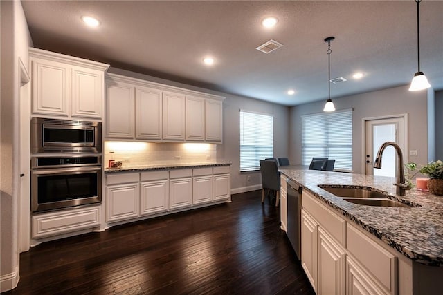 kitchen featuring decorative light fixtures, sink, appliances with stainless steel finishes, an island with sink, and white cabinets