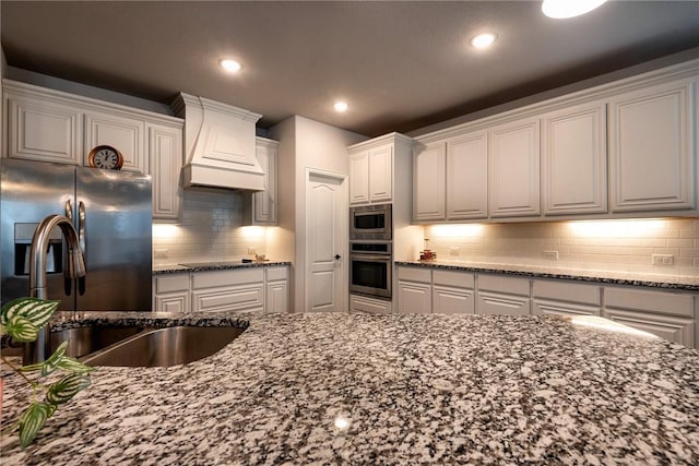 kitchen with premium range hood, stainless steel appliances, stone counters, white cabinets, and sink