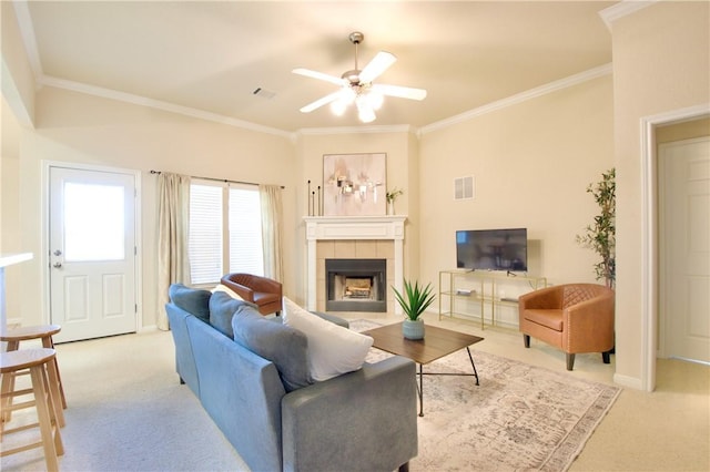 living room featuring a tiled fireplace, crown molding, ceiling fan, and light colored carpet